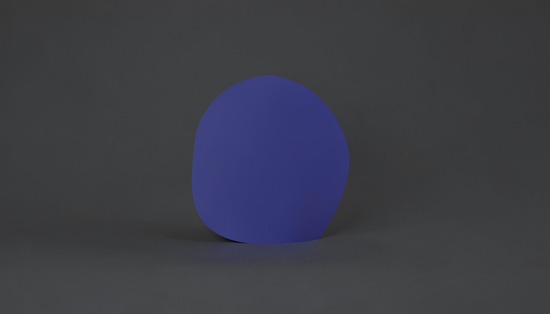 A minimalist studio photograph with a charcoal gray background and a single soft indigo accent shape, understated and calm in style